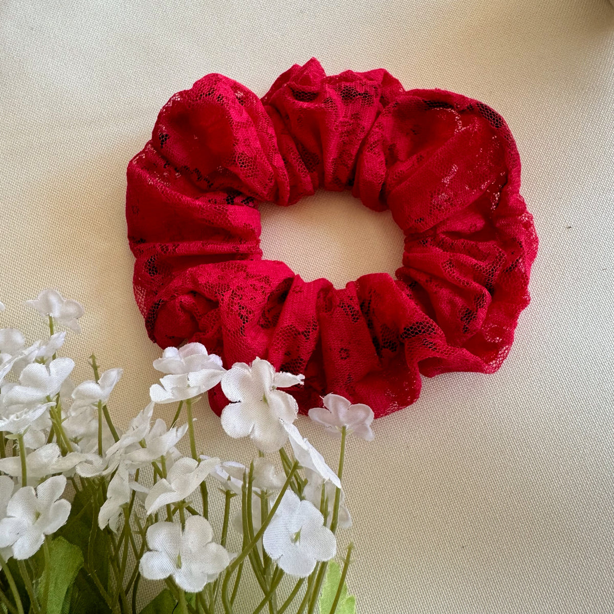 Red lace scrunchie on a beige background with white flowers.