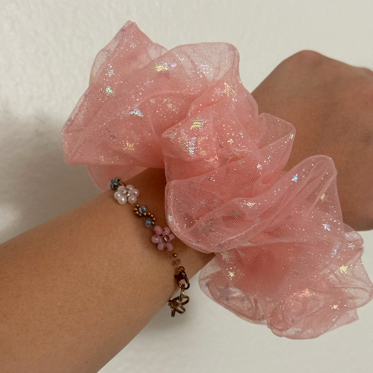 Pink scrunchie on a wrist with a white background