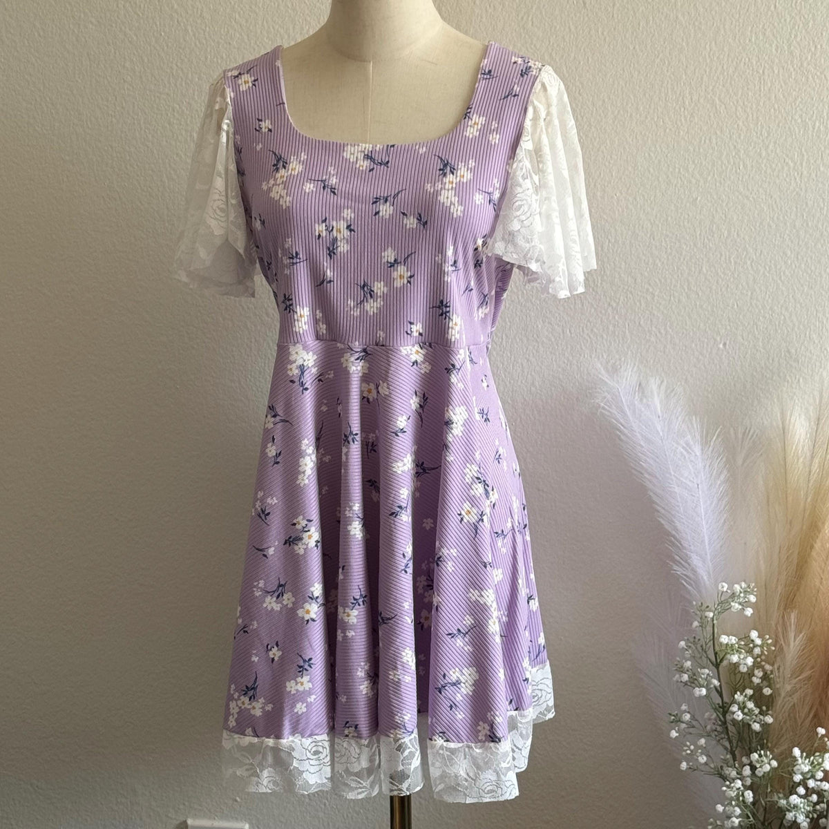 Purple floral dress with white lace sleeves on a mannequin against a neutral background