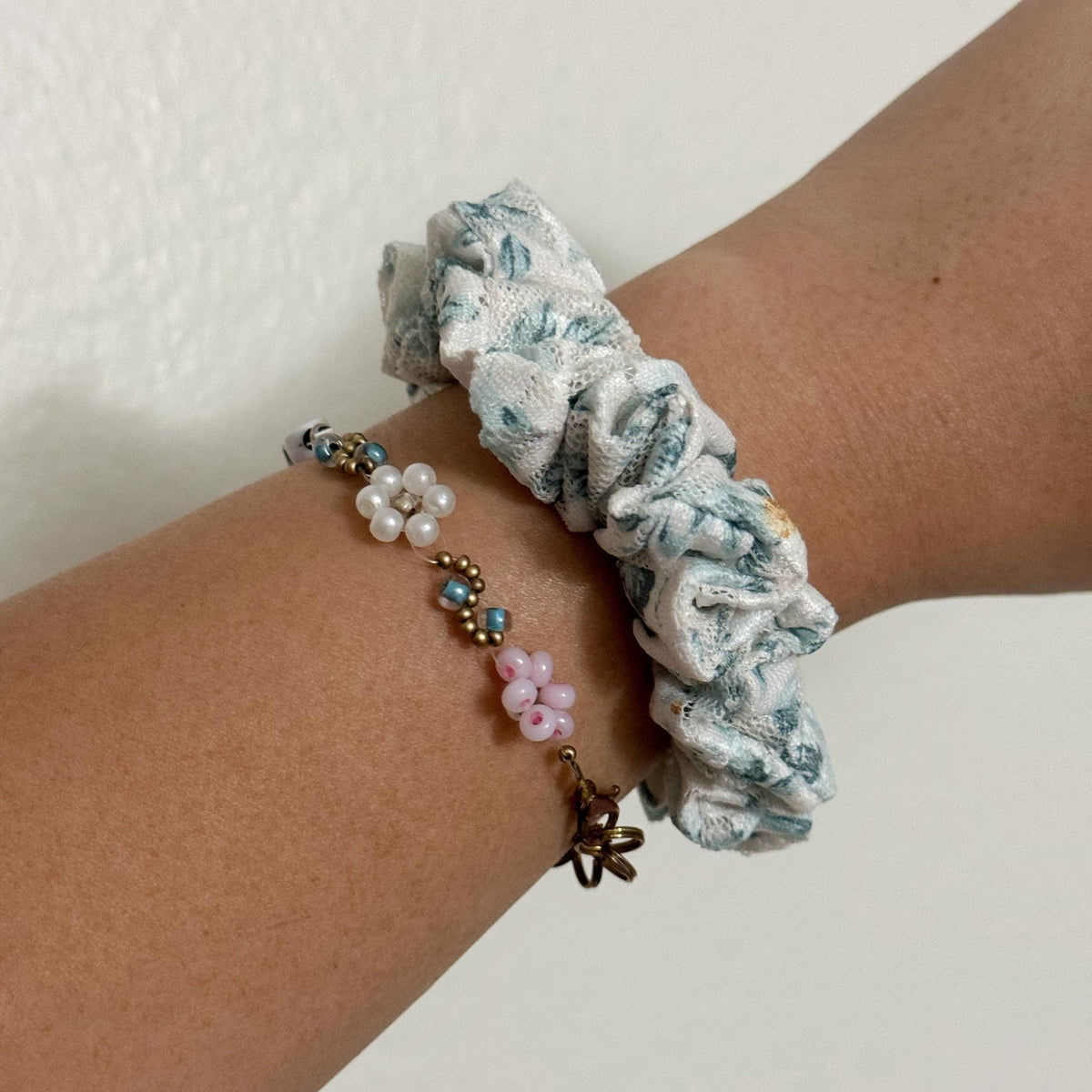 Wrist wearing a floral scrunchie and beaded bracelet on a plain background