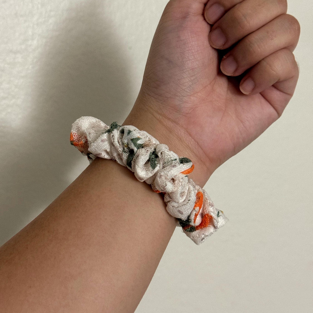 Hand wearing a floral scrunchie on a plain background